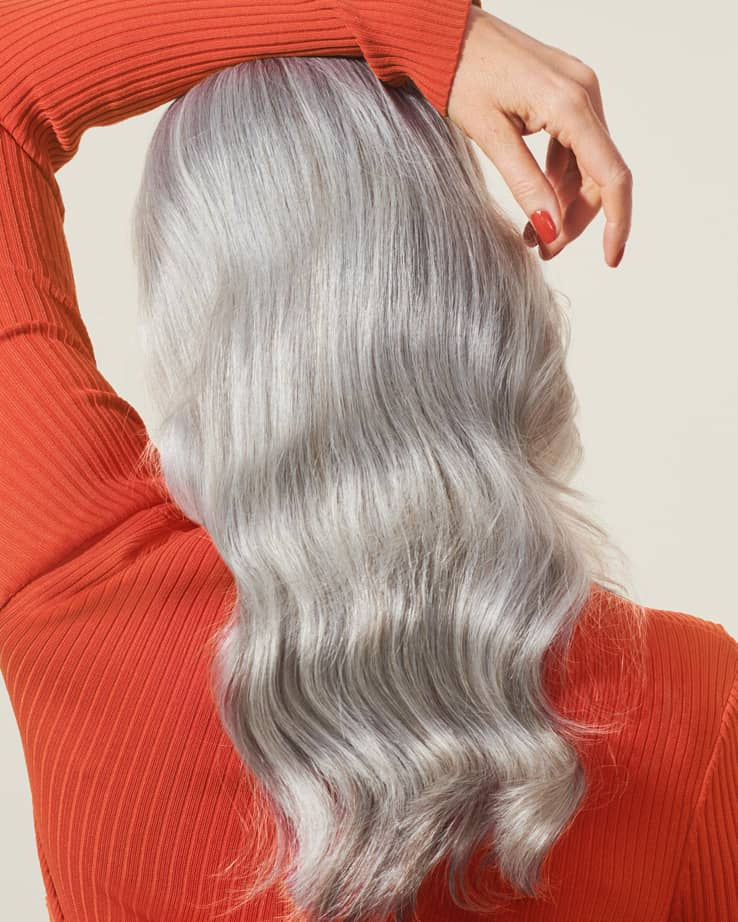 Woman with red sweater and beautiful and wavy white hair photographed from behind on beige background