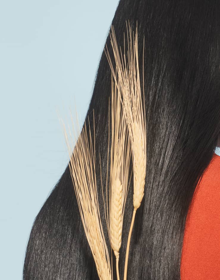 Blong wavy haired woman similing holding a few pieces of millet in front of her face on beige background