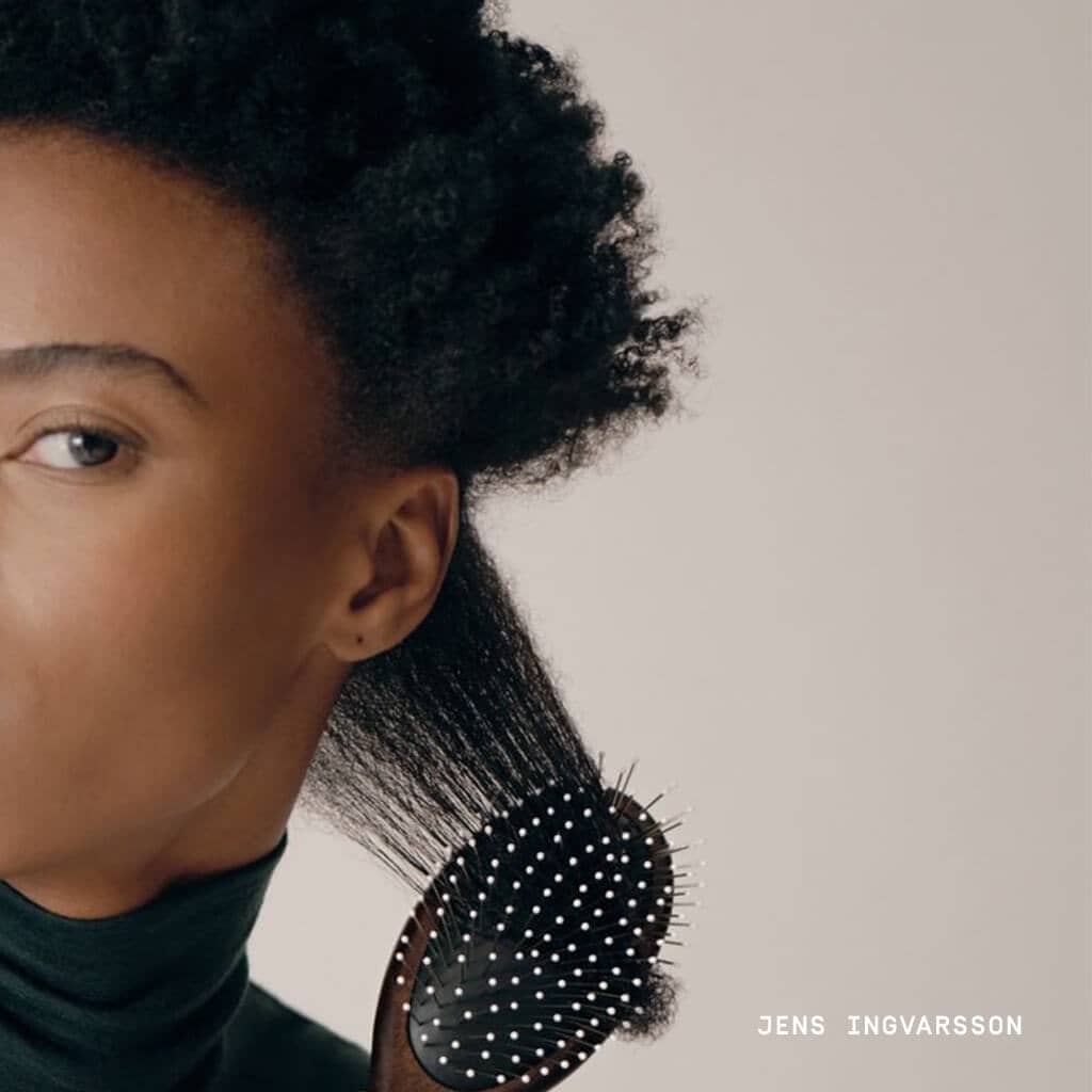 brown hair woman in green turtleneck brushing through a section of hair
