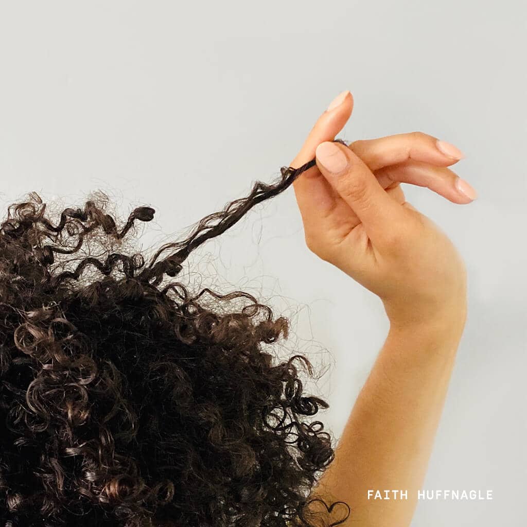 Woman holding curl in between fingers with brown curly hair